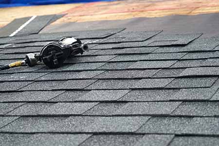 nail gun laying on asphalt roof that is being installed